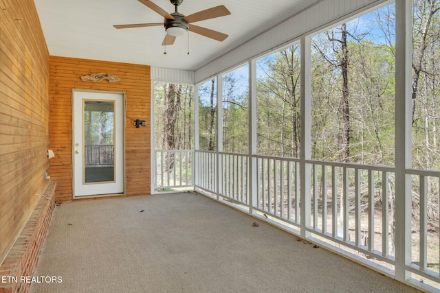 unfurnished sunroom with wooden walls, a ceiling fan, plenty of natural light, and carpet