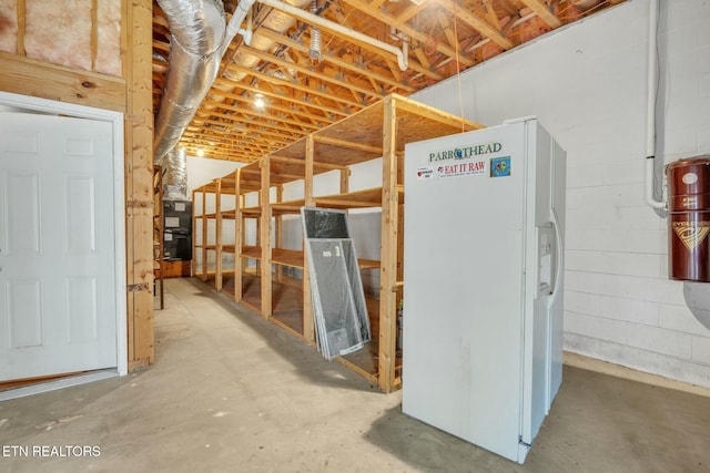 below grade area featuring white refrigerator with ice dispenser and concrete block wall