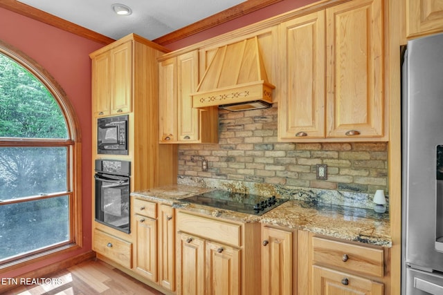 kitchen with custom exhaust hood, light brown cabinetry, black appliances, light stone countertops, and decorative backsplash