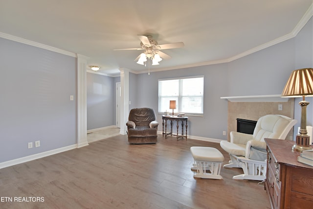 living area with crown molding, ceiling fan, a tiled fireplace, and wood finished floors