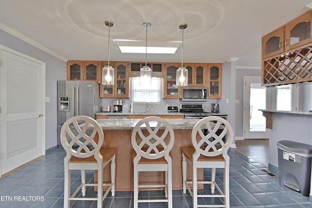 kitchen featuring dark tile patterned floors, appliances with stainless steel finishes, a kitchen island, and brown cabinets