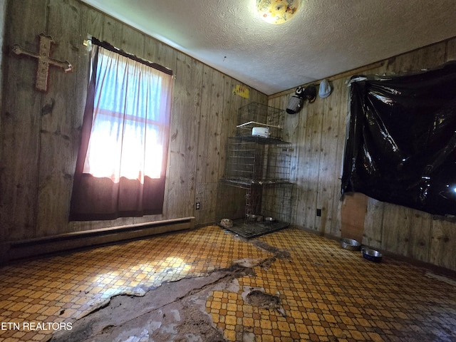 empty room featuring tile patterned floors, baseboard heating, wood walls, and a textured ceiling