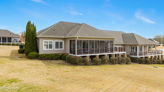 rear view of property featuring a lawn, a sunroom, and roof with shingles