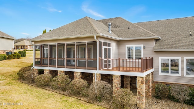 rear view of property with a sunroom, roof with shingles, and a lawn