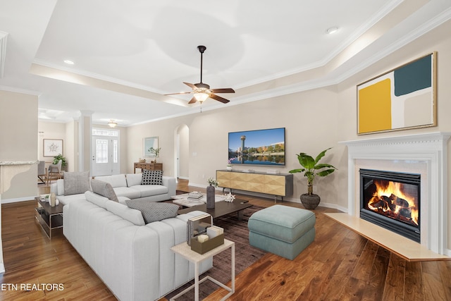 living area with a fireplace with flush hearth, wood-type flooring, arched walkways, ceiling fan, and ornamental molding
