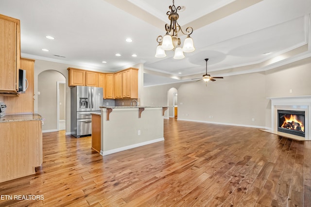 kitchen featuring light wood finished floors, a kitchen bar, stainless steel appliances, arched walkways, and ceiling fan with notable chandelier