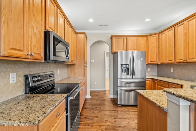 kitchen featuring light stone counters, light wood-type flooring, stainless steel appliances, visible vents, and arched walkways