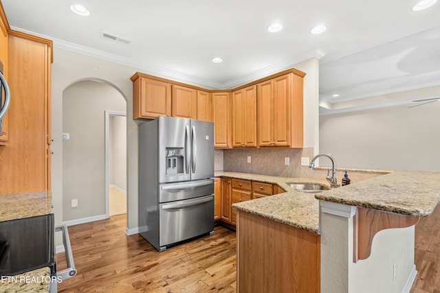 kitchen with crown molding, a sink, stainless steel fridge, a peninsula, and arched walkways