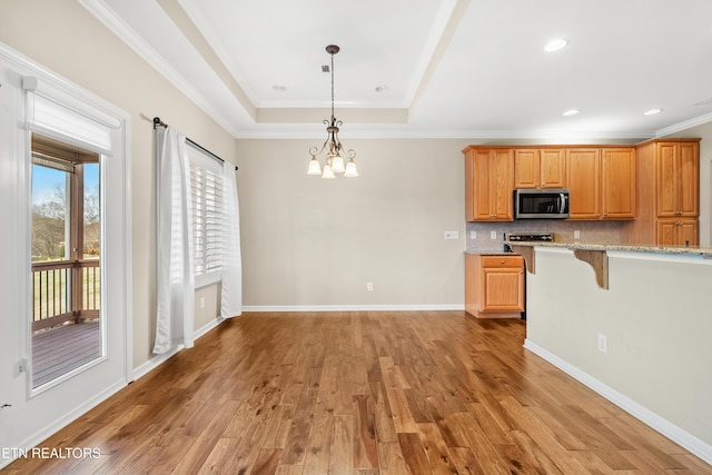 kitchen featuring light wood-style flooring, a chandelier, stainless steel microwave, a raised ceiling, and backsplash