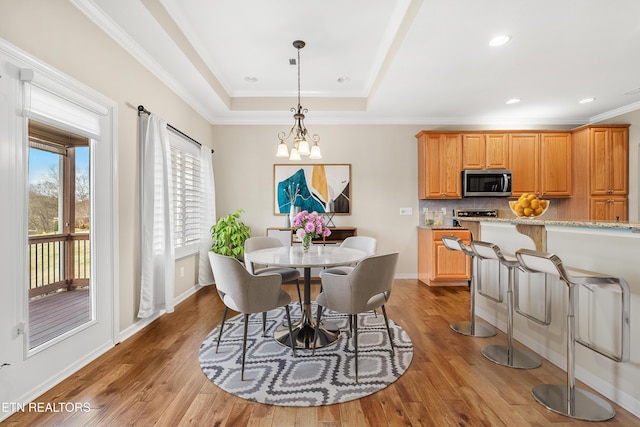 dining area with a tray ceiling, baseboards, wood finished floors, and ornamental molding