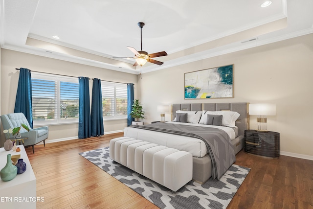 bedroom featuring a tray ceiling, baseboards, visible vents, and wood finished floors