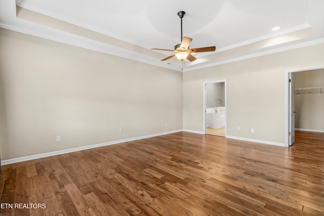 unfurnished bedroom featuring baseboards, wood finished floors, a walk in closet, and a raised ceiling