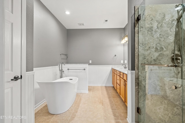 bathroom featuring vanity, a stall shower, a freestanding bath, tile patterned flooring, and wainscoting