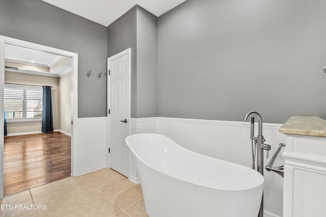 full bathroom with wainscoting, a freestanding bath, tile patterned flooring, and a raised ceiling