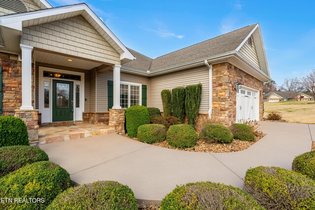 view of exterior entry featuring stone siding, an attached garage, concrete driveway, and a porch