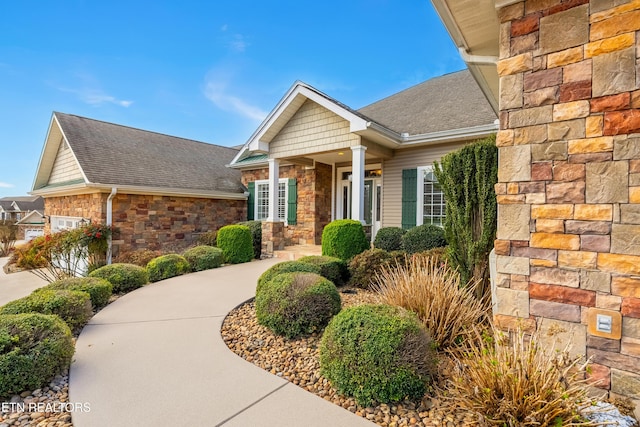 view of front of property with stone siding, an attached garage, and a shingled roof