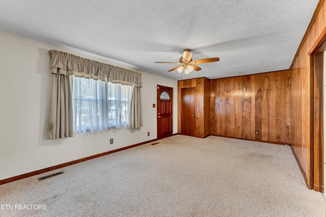 unfurnished room featuring wooden walls, visible vents, light carpet, a textured ceiling, and a ceiling fan