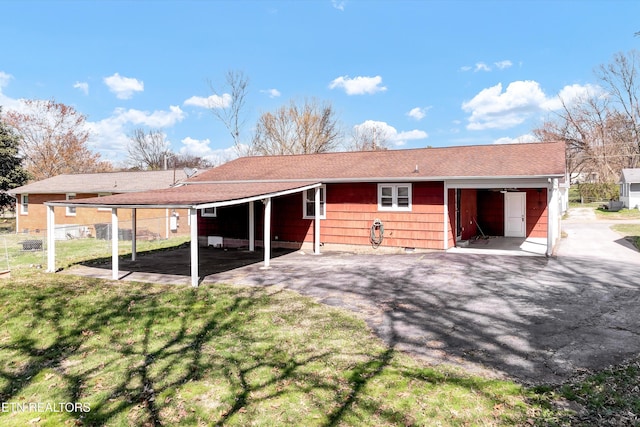 back of property with a carport, a lawn, and aphalt driveway