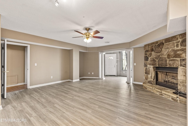 221 Woodland Rd Unit 315, Gatlinburg, TN 37738 - unfurnished living room featuring a textured ceiling, a ceiling fan, a stone fireplace, light wood finished floors, and baseboards