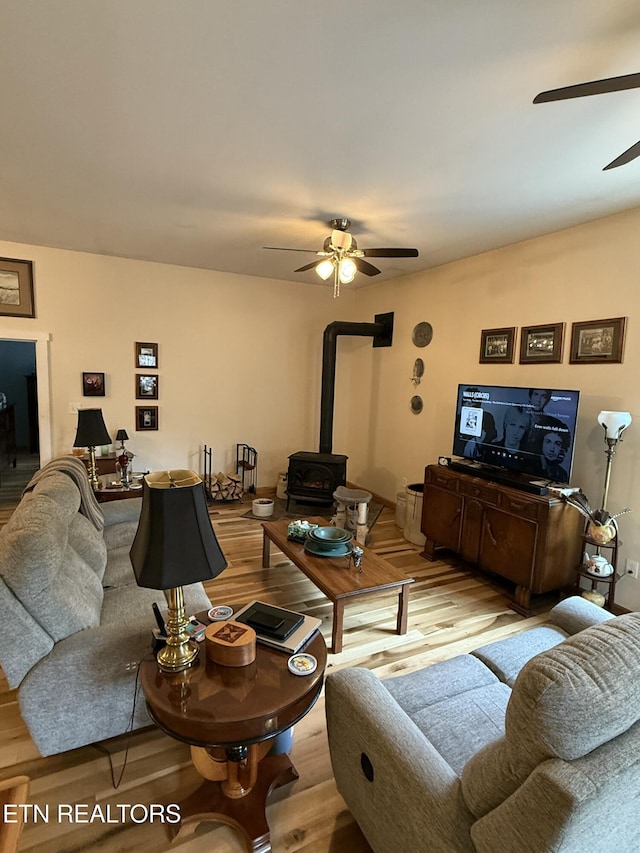 living area featuring wood finished floors, a wood stove, and a ceiling fan