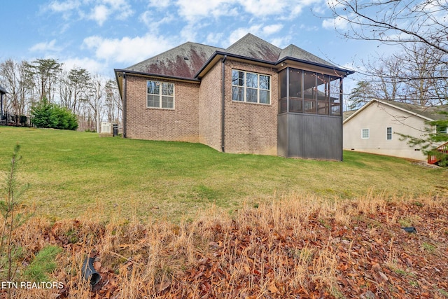 back of house featuring a lawn, brick siding, and a sunroom