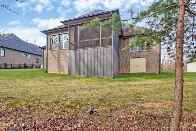 back of house with a lawn, a sunroom, and brick siding