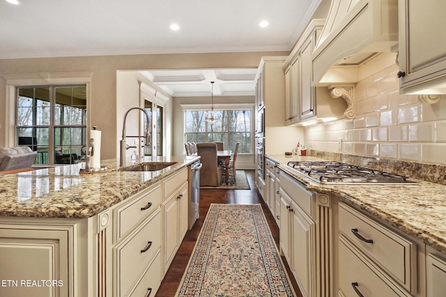 kitchen featuring under cabinet range hood, cream cabinets, a sink, dark wood-style floors, and appliances with stainless steel finishes