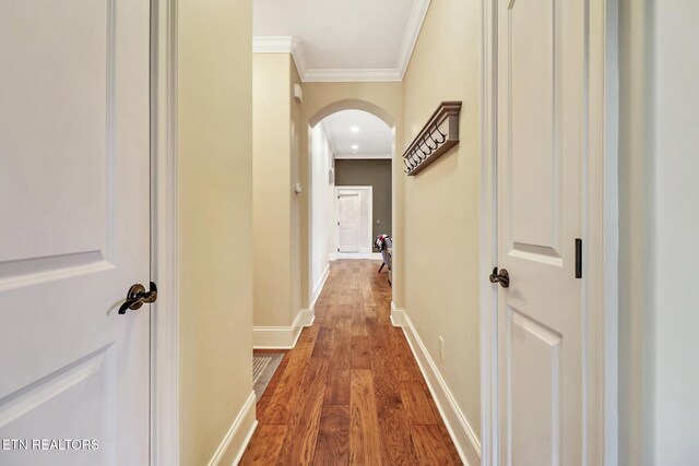 corridor with arched walkways, dark wood-style floors, baseboards, and crown molding