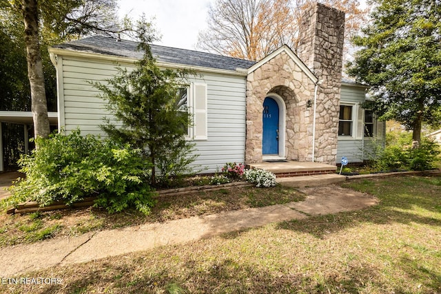 view of front of house featuring stone siding, a chimney, a front yard, an attached carport, and roof with shingles