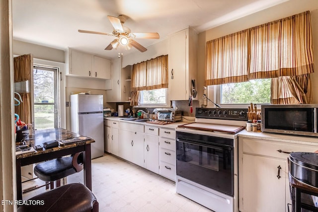 kitchen with stainless steel microwave, light floors, a sink, electric range oven, and freestanding refrigerator