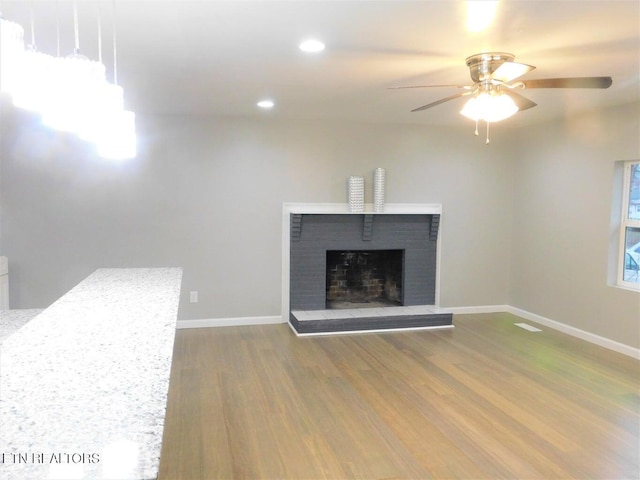 unfurnished living room with a brick fireplace, baseboards, wood finished floors, recessed lighting, and a ceiling fan