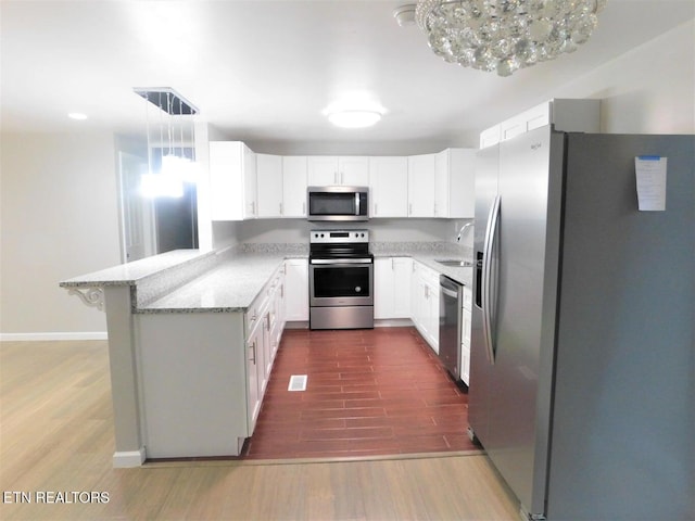 kitchen with light stone countertops, appliances with stainless steel finishes, a peninsula, visible vents, and dark wood-type flooring