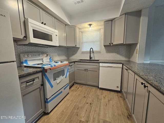 kitchen with a sink, white appliances, tasteful backsplash, light wood-type flooring, and gray cabinetry