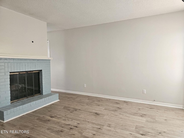 unfurnished living room featuring a textured ceiling, wood finished floors, baseboards, and a fireplace