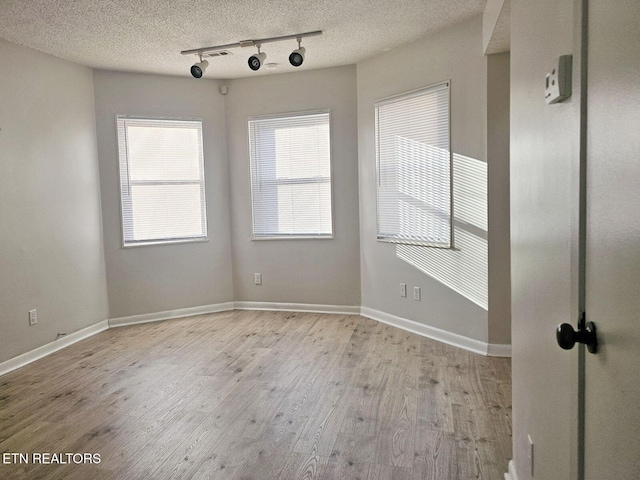 spare room with rail lighting, a textured ceiling, wood finished floors, and baseboards