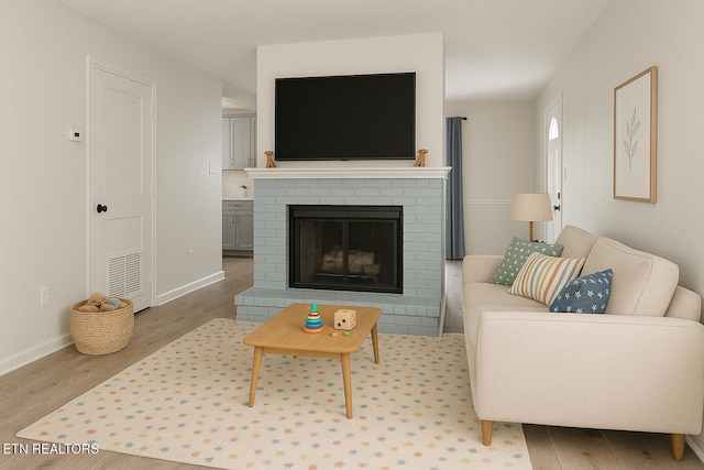 living room with light wood-style floors, visible vents, baseboards, and a brick fireplace