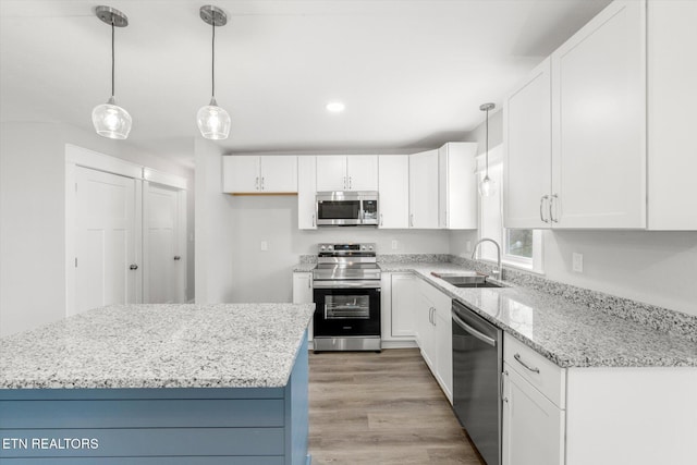 kitchen with light wood finished floors, stainless steel appliances, a sink, white cabinetry, and light stone countertops