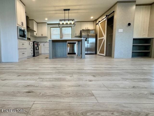 kitchen featuring white cabinetry, a barn door, wall chimney exhaust hood, open floor plan, and stainless steel appliances