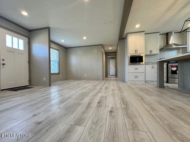 interior space featuring light wood finished floors, wall chimney exhaust hood, white cabinets, and stainless steel microwave