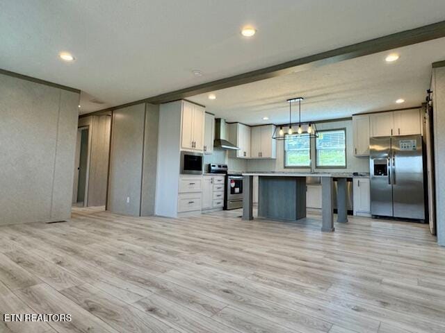 kitchen with a kitchen bar, light wood-type flooring, stainless steel appliances, wall chimney range hood, and white cabinets