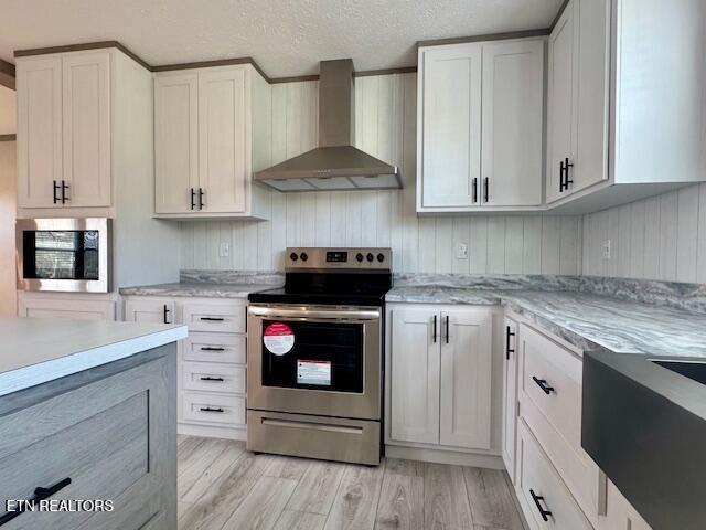 kitchen with white cabinets, stainless steel appliances, light wood-style floors, and wall chimney exhaust hood