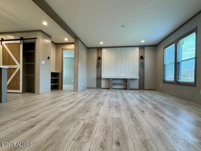 unfurnished living room featuring crown molding, a barn door, wood finished floors, and recessed lighting