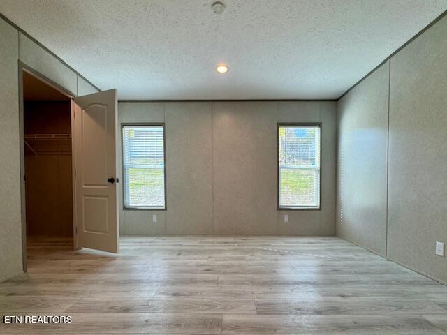 unfurnished bedroom with a closet, a textured ceiling, a spacious closet, and light wood finished floors
