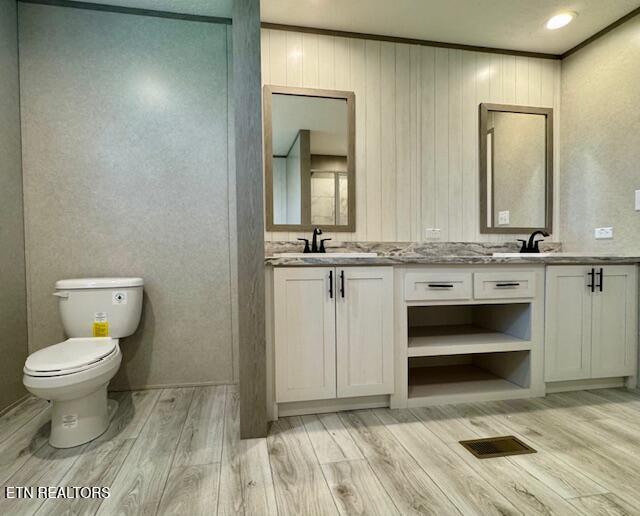 full bath with toilet, a sink, wood finished floors, visible vents, and double vanity