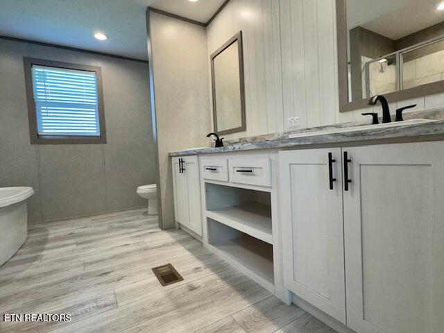 bathroom featuring toilet, a shower stall, wood finished floors, visible vents, and double vanity