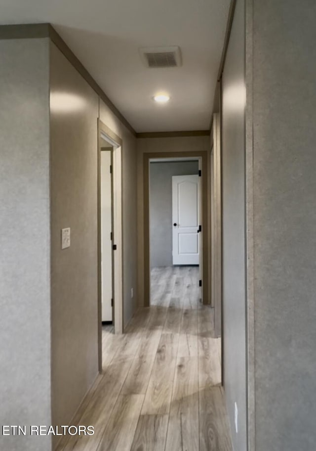 hall featuring visible vents, light wood-style flooring, and ornamental molding