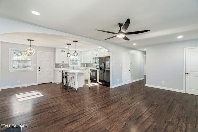 unfurnished living room with dark wood-type flooring, a wealth of natural light, baseboards, and ceiling fan with notable chandelier