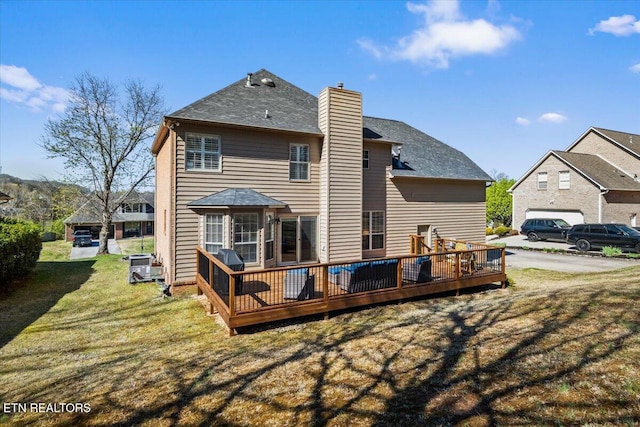rear view of property featuring a lawn, a chimney, a shingled roof, and a deck