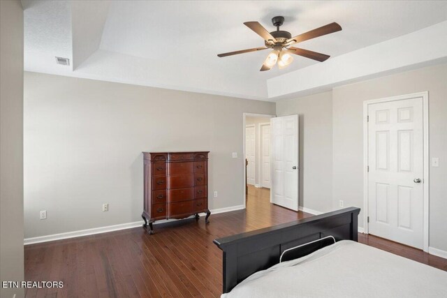 unfurnished bedroom featuring dark wood-style flooring, visible vents, baseboards, ceiling fan, and a tray ceiling