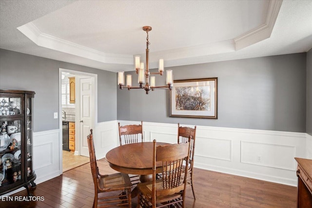 dining space featuring a wainscoted wall, a textured ceiling, a tray ceiling, dark wood-style floors, and a notable chandelier